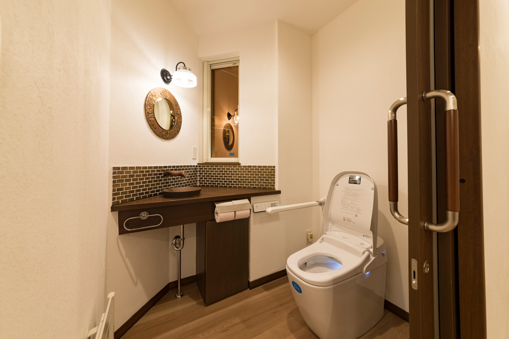 World-inspired cloakroom in Other with white walls, light hardwood flooring, a vessel sink and brown floors.