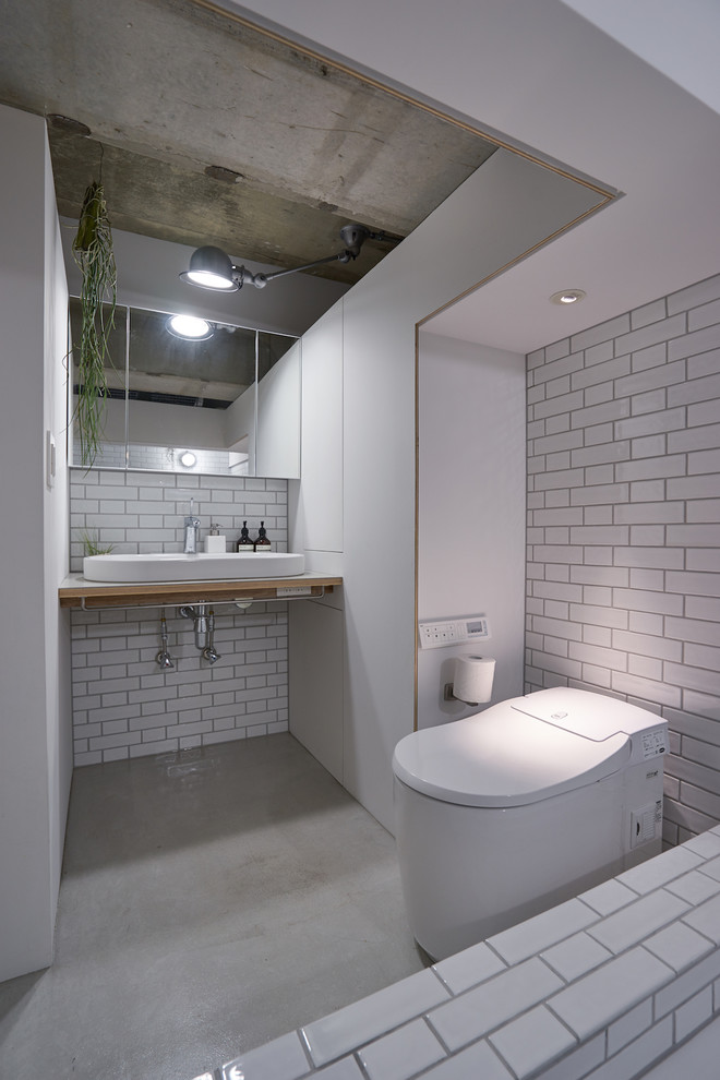 東京23区にあるインダストリアルスタイルのおしゃれなトイレ・洗面所 (白いタイル、白い壁、コンクリートの床、ベッセル式洗面器、木製洗面台、グレーの床、ブラウンの洗面カウンター) の写真