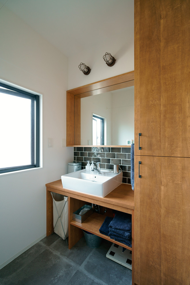 Cette photo montre un WC et toilettes scandinave avec un placard à porte plane, des portes de placard marrons, un mur blanc, une vasque, un plan de toilette en bois, un sol noir et un plan de toilette marron.