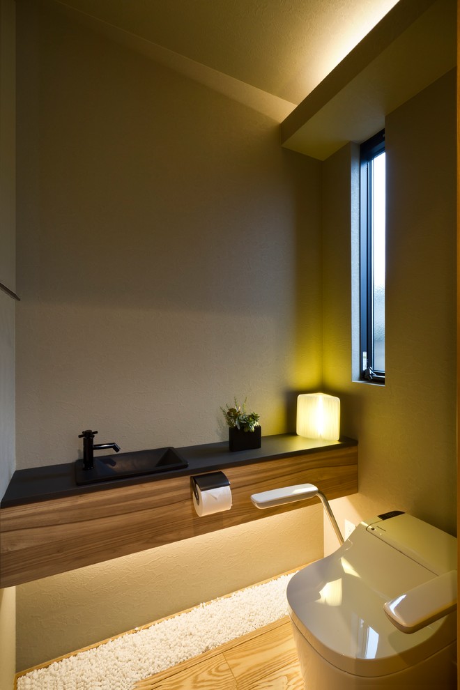 Modern inredning av ett toalett, med bruna väggar, mellanmörkt trägolv, ett nedsänkt handfat och brunt golv