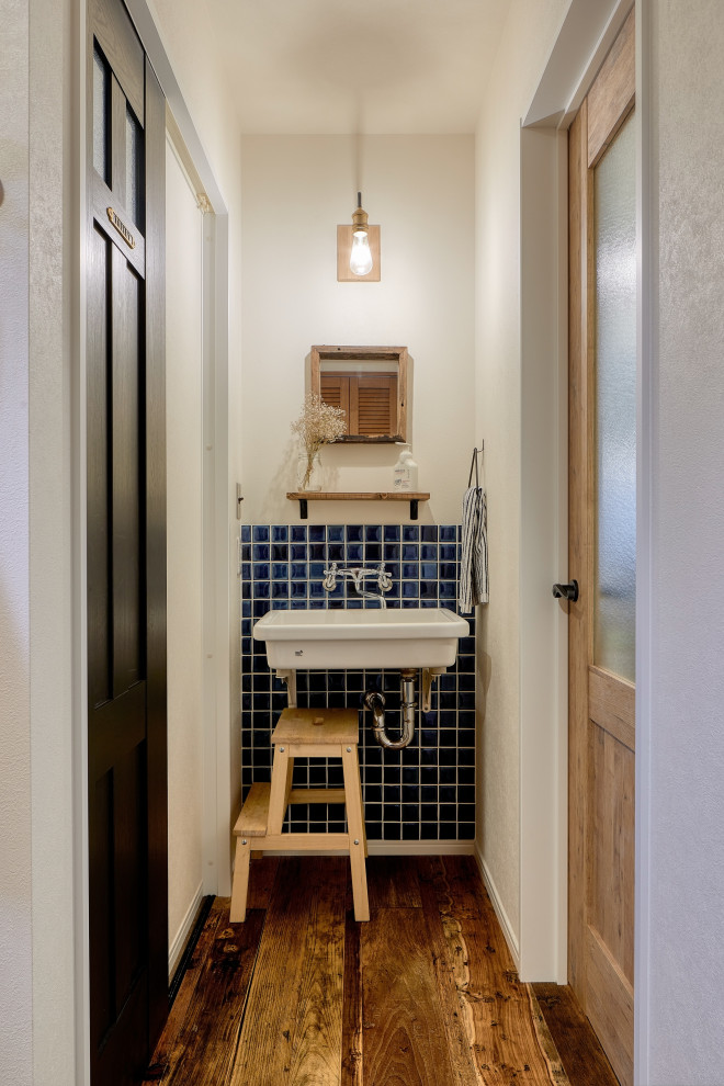 Idéer för att renovera ett litet minimalistiskt brun brunt toalett, med öppna hyllor, vita skåp, en vägghängd toalettstol, blå kakel, glaskakel, vita väggar, plywoodgolv, ett väggmonterat handfat, bänkskiva i kvarts och brunt golv
