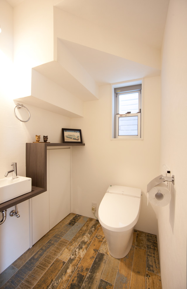 Modern inredning av ett brun brunt toalett, med släta luckor, vita skåp, vita väggar, målat trägolv, ett fristående handfat, träbänkskiva och brunt golv