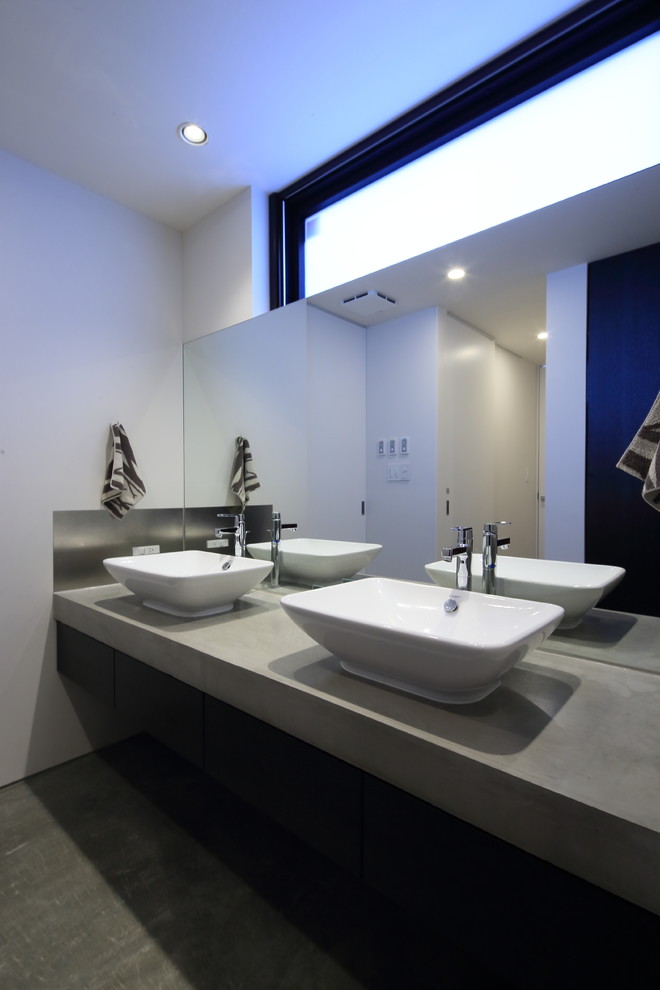 Imagen de aseo moderno con paredes blancas, lavabo sobreencimera, encimera de cemento y suelo gris