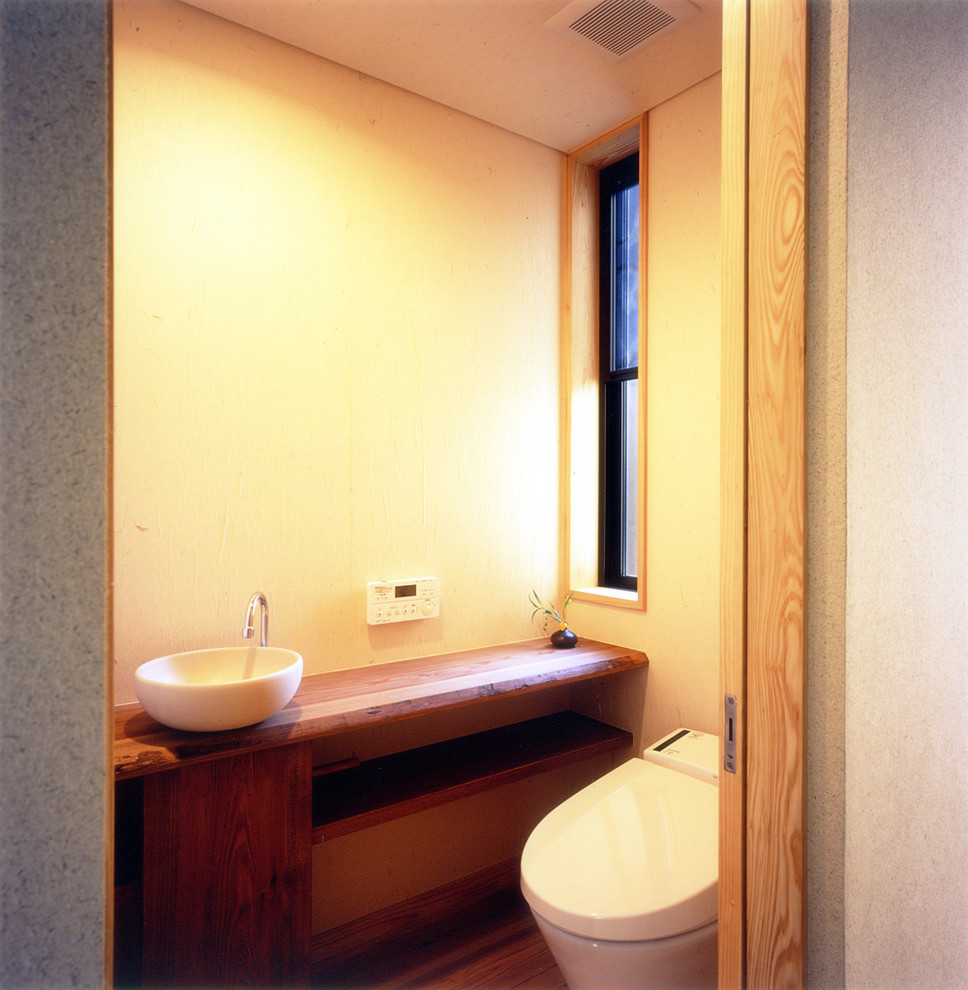 Idee per un bagno di servizio etnico con ante in legno scuro, WC monopezzo, pareti beige, parquet chiaro, lavabo a bacinella e pavimento marrone
