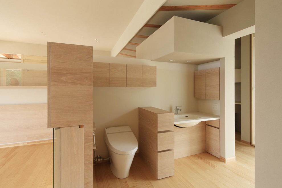Immagine di un bagno di servizio minimalista con ante lisce, ante in legno chiaro, WC monopezzo, pareti beige, parquet chiaro e lavabo integrato