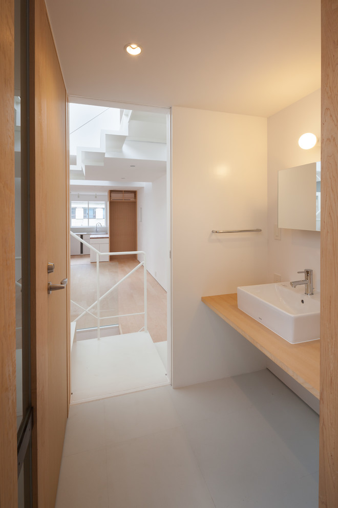 Пример оригинального дизайна: туалет среднего размера в стиле модернизм с унитазом-моноблоком, белой плиткой, белыми стенами, полом из линолеума, настольной раковиной и столешницей из дерева