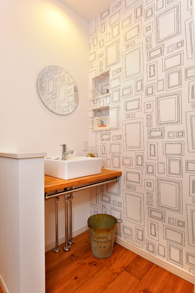 Skandinavische Gästetoilette mit weißer Wandfarbe, braunem Holzboden, Aufsatzwaschbecken, Waschtisch aus Holz, braunem Boden und brauner Waschtischplatte in Sonstige