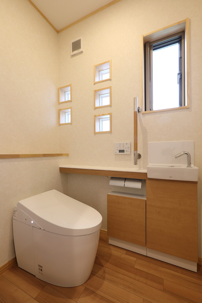 Cette photo montre un WC et toilettes en bois clair de taille moyenne avec un placard en trompe-l'oeil, WC à poser, un mur blanc, un sol en contreplaqué, un lavabo intégré, un plan de toilette en surface solide, un sol beige et un plan de toilette blanc.
