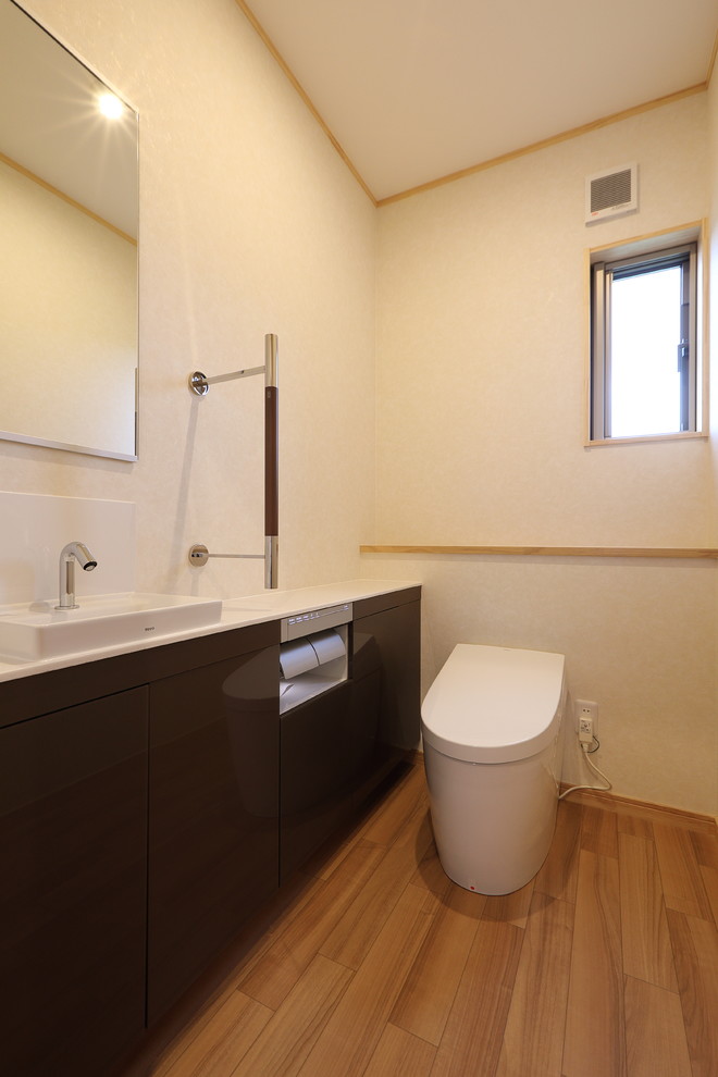 Aménagement d'un grand WC et toilettes en bois clair avec un placard en trompe-l'oeil, WC à poser, un mur blanc, un sol en contreplaqué, une vasque, un plan de toilette en surface solide, un sol beige et un plan de toilette blanc.