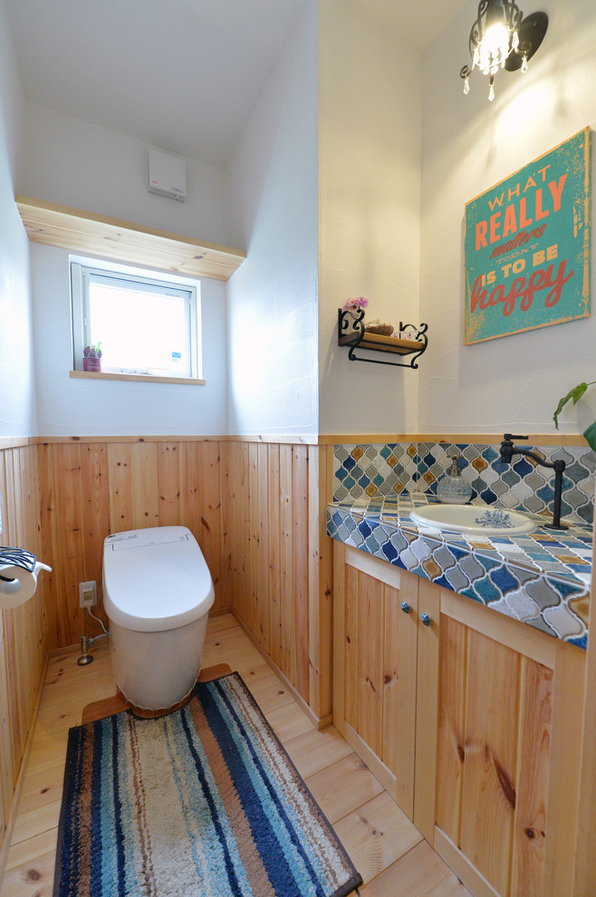 Idées déco pour un WC et toilettes campagne en bois brun avec un placard avec porte à panneau encastré, un mur blanc, un sol en bois brun, un lavabo posé, un plan de toilette en carrelage et un sol marron.