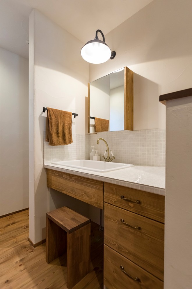 Inredning av ett eklektiskt vit vitt toalett, med möbel-liknande, skåp i mörkt trä, vit kakel, vita väggar, mörkt trägolv, kaklad bänkskiva och brunt golv