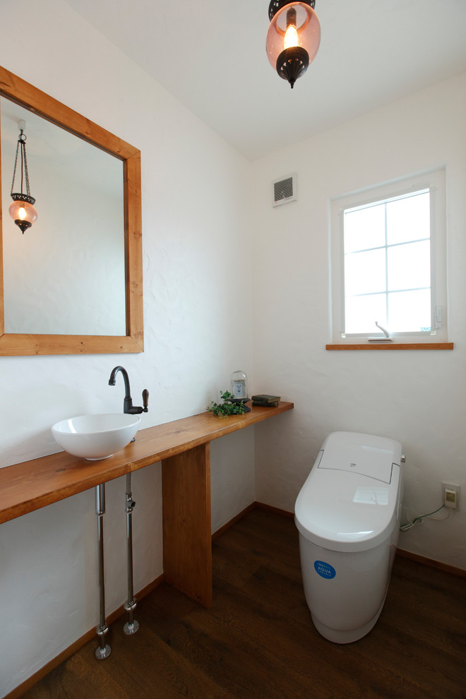 Cette photo montre un WC et toilettes méditerranéen avec un placard sans porte, un mur blanc, parquet foncé, une vasque, un plan de toilette en bois, un sol marron et un plan de toilette marron.