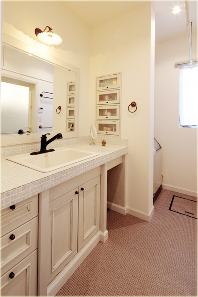 Aménagement d'un WC et toilettes classique avec un placard avec porte à panneau encastré, des portes de placard blanches, un mur blanc, un plan de toilette en carrelage et un sol marron.