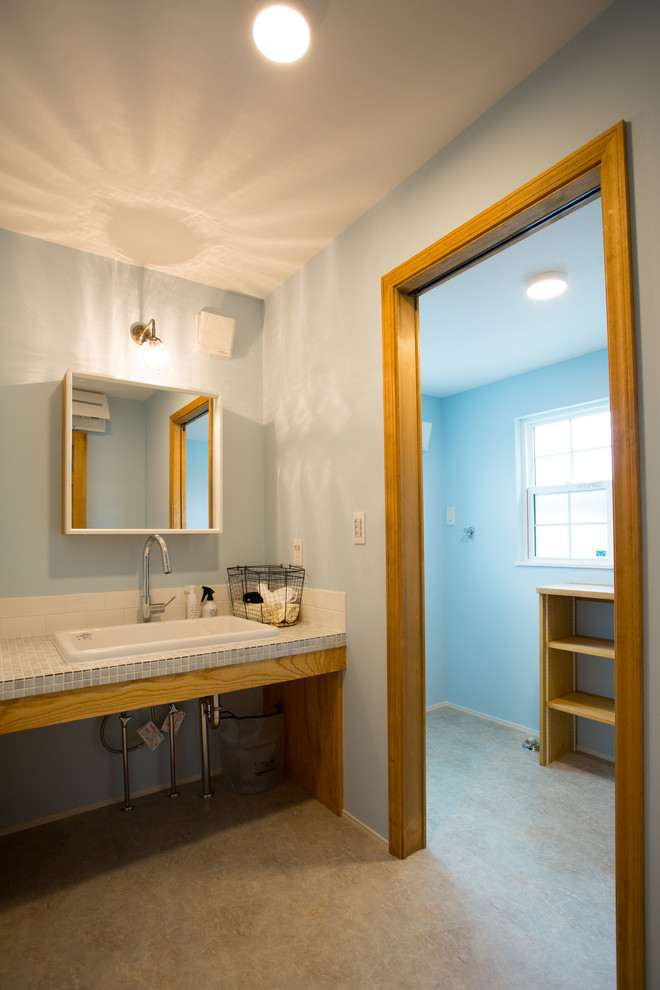 Modelo de aseo de estilo de casa de campo con paredes azules, suelo de cemento, lavabo encastrado, encimera de azulejos, suelo gris y encimeras azules