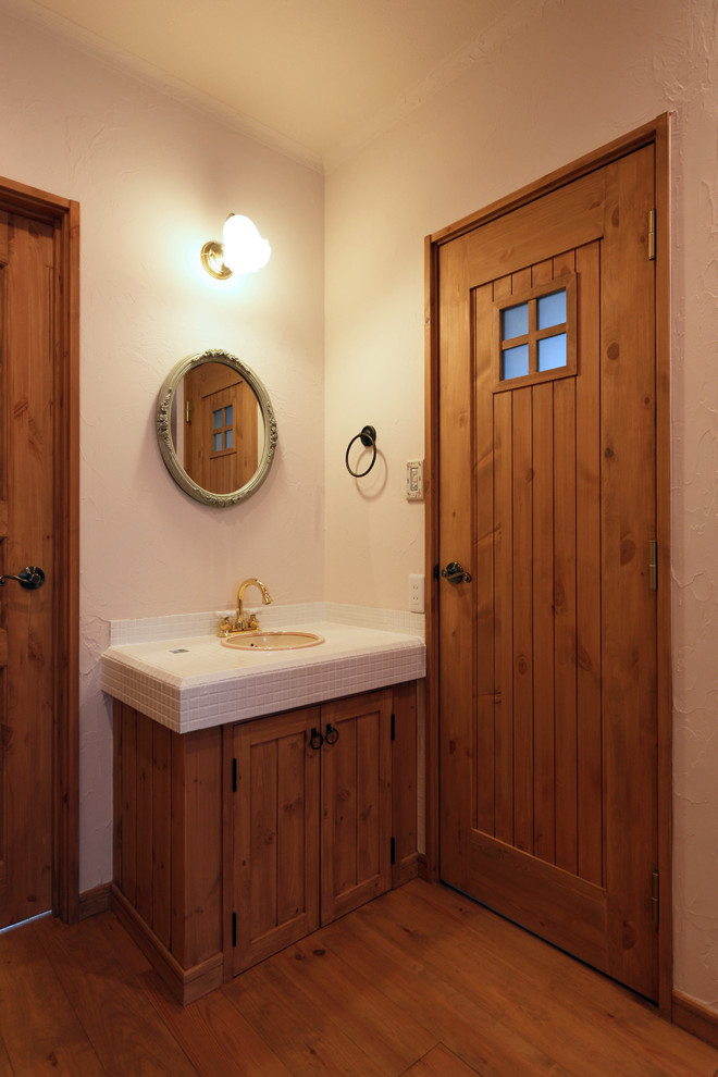 他の地域にある北欧スタイルのおしゃれなトイレ・洗面所 (中間色木目調キャビネット、白い壁、無垢フローリング、オーバーカウンターシンク、タイルの洗面台、茶色い床) の写真