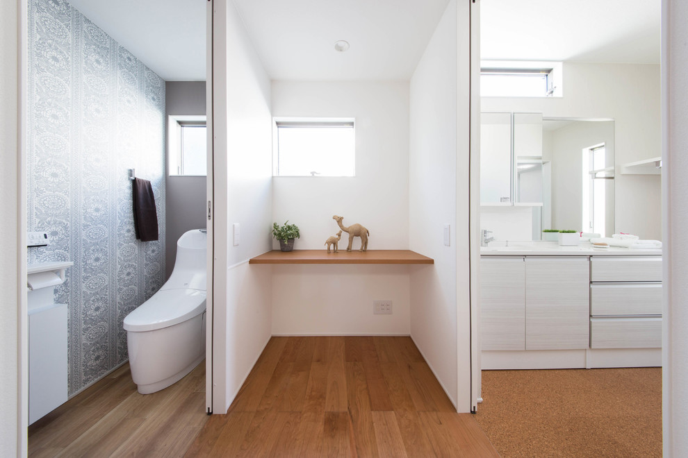 Idée de décoration pour un WC et toilettes minimaliste avec un placard à porte plane, des portes de placard blanches, WC à poser, un mur blanc, un sol en liège, un lavabo intégré, un sol marron et un plan de toilette blanc.