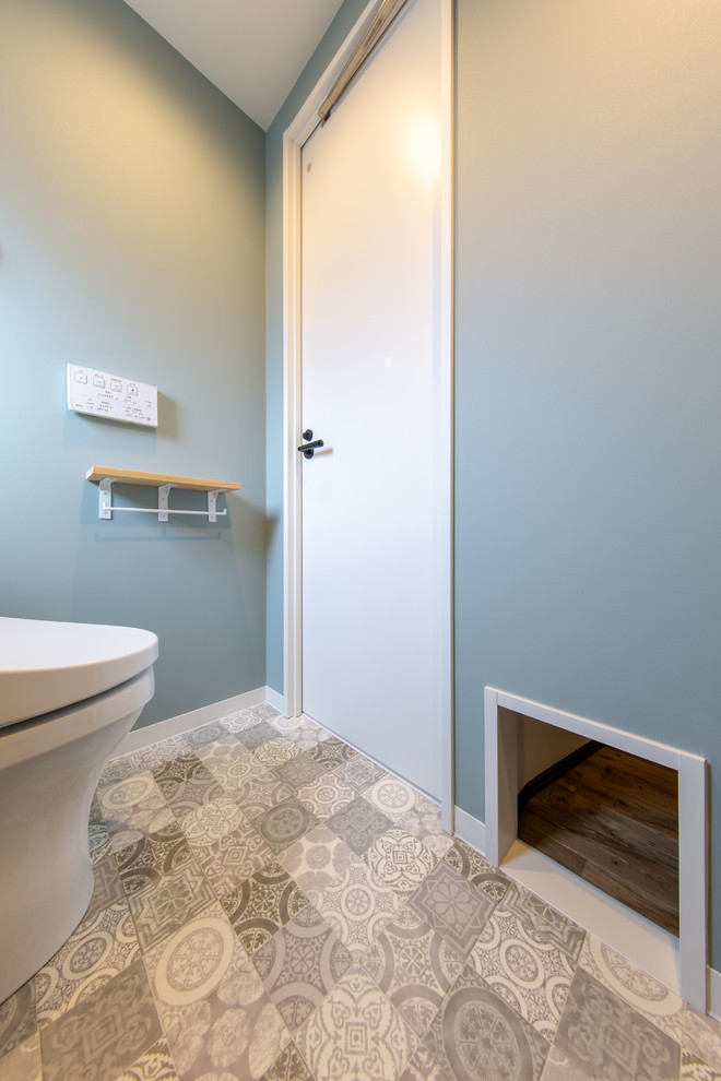 Mittelgroße Shabby-Chic Gästetoilette mit Schränken im Used-Look, Toilette mit Aufsatzspülkasten, blauer Wandfarbe, braunem Holzboden und buntem Boden in Tokio