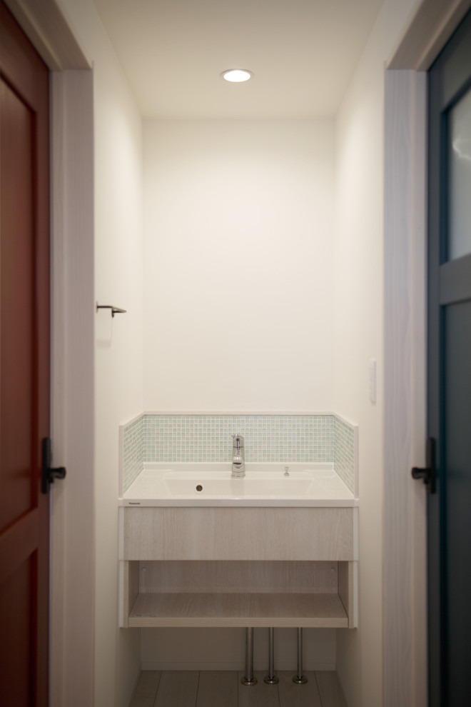 Skandinavische Gästetoilette mit blauen Fliesen, Glasfliesen, gelber Wandfarbe, integriertem Waschbecken und weißer Waschtischplatte in Sonstige
