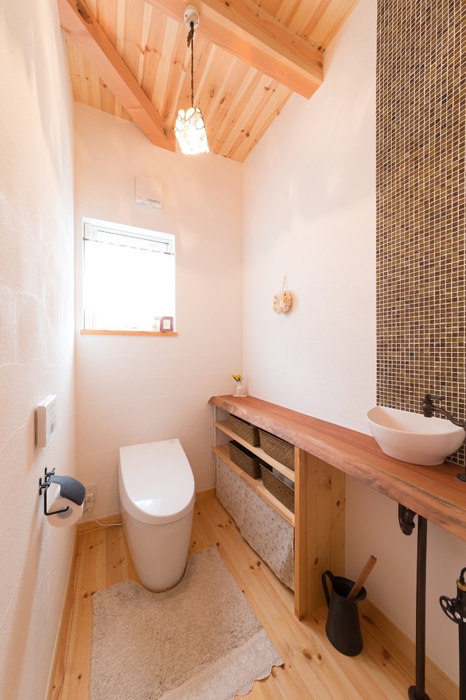 Inredning av ett asiatiskt brun brunt toalett, med öppna hyllor, brun kakel, vita väggar, ljust trägolv, ett fristående handfat, träbänkskiva och brunt golv