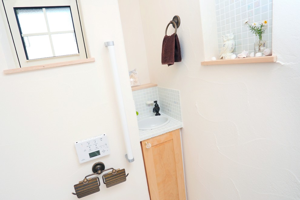 Cette image montre un petit WC et toilettes rustique en bois clair avec un placard à porte affleurante, WC à poser, un carrelage blanc, mosaïque, un mur blanc, un sol en linoléum, un lavabo posé, un plan de toilette en carrelage et un sol beige.