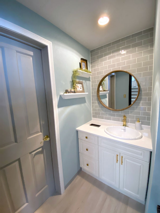Cette image montre un petit WC et toilettes style shabby chic avec un placard à porte affleurante, des portes de placard blanches, des carreaux de porcelaine, un mur bleu, un sol beige, un plan de toilette blanc, meuble-lavabo sur pied et un carrelage gris.