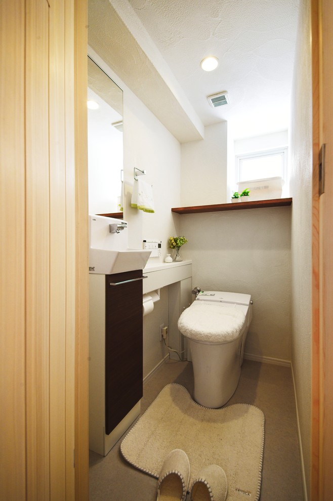 Cette image montre un WC et toilettes nordique avec un placard à porte plane, des portes de placard marrons, un mur blanc, une vasque et un sol gris.