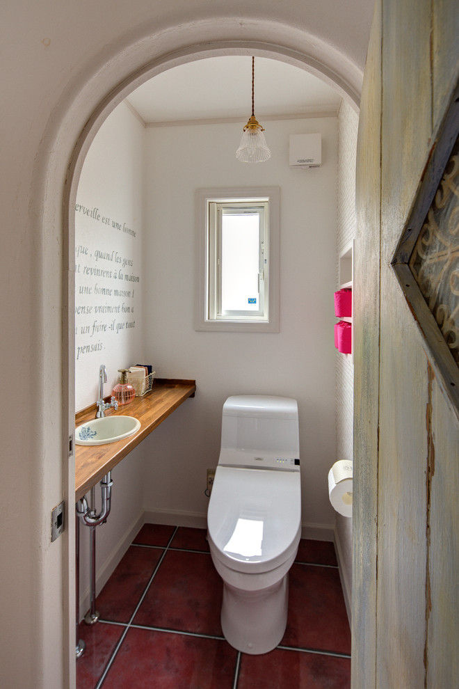 東京都下にあるトランジショナルスタイルのおしゃれなトイレ・洗面所 (白い壁、テラコッタタイルの床、オーバーカウンターシンク、木製洗面台、赤い床、ブラウンの洗面カウンター) の写真
