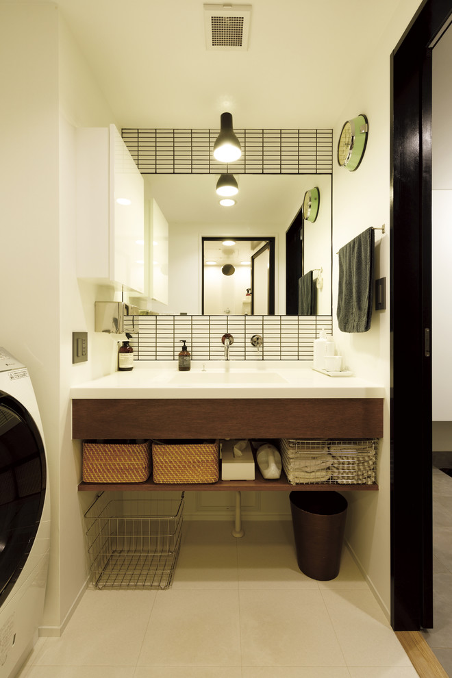 東京23区にあるアジアンスタイルのおしゃれなトイレ・洗面所 (フラットパネル扉のキャビネット、濃色木目調キャビネット、白いタイル、白い壁、一体型シンク、ベージュの床、白い洗面カウンター) の写真