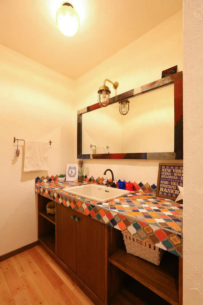 Exemple d'un WC et toilettes éclectique avec mosaïque, un mur blanc, parquet clair, un lavabo posé, un plan de toilette en carrelage, un sol beige, un placard à porte affleurante, des portes de placard marrons et un carrelage blanc.