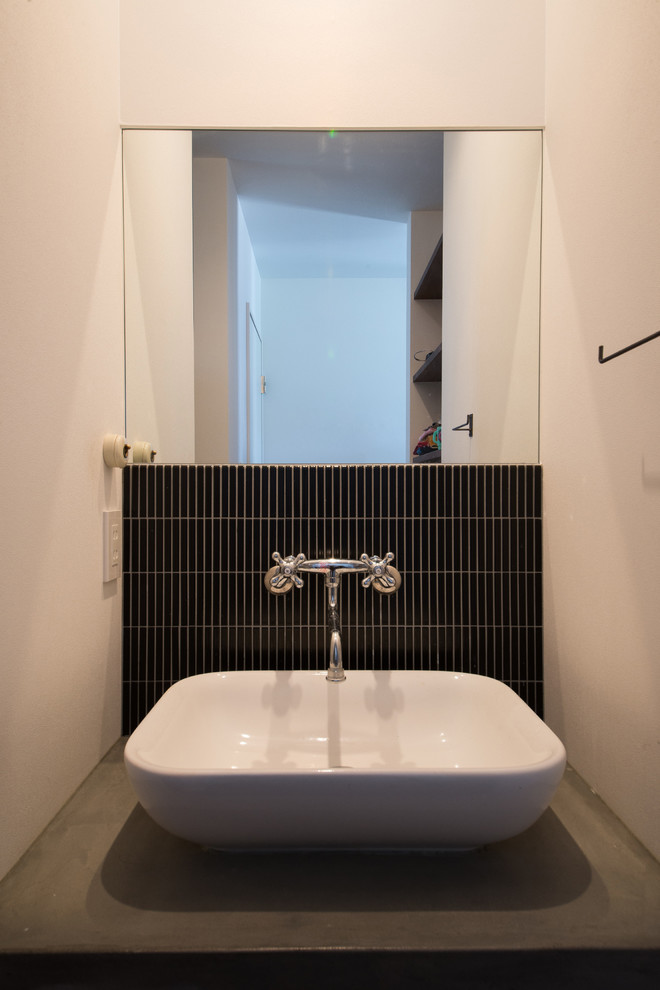 他の地域にあるインダストリアルスタイルのおしゃれなトイレ・洗面所 (黒いタイル、磁器タイル、白い壁、コンクリートの洗面台) の写真