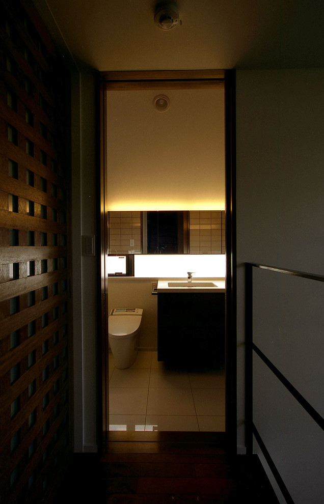 Inspiration for a medium sized modern cloakroom in Tokyo with flat-panel cabinets, dark wood cabinets, a one-piece toilet, ceramic tiles, white walls, porcelain flooring, a submerged sink, solid surface worktops, beige tiles, white worktops and white floors.
