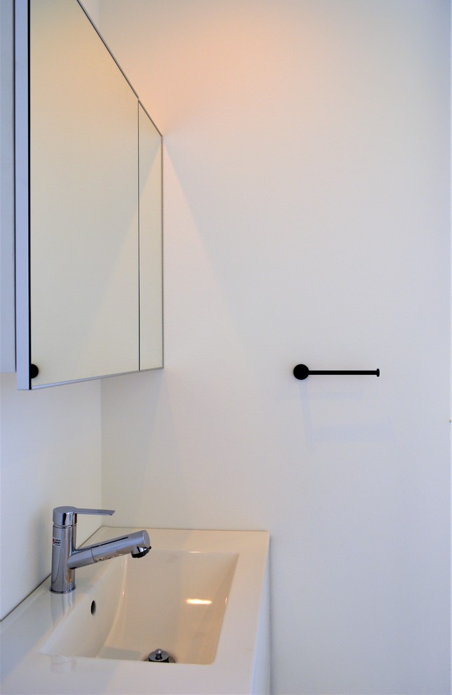 Cette photo montre un WC et toilettes moderne avec un placard à porte affleurante, des portes de placard noires, un carrelage blanc, un mur blanc, un sol en contreplaqué, un lavabo posé, un plan de toilette en surface solide, un sol blanc et un plan de toilette noir.