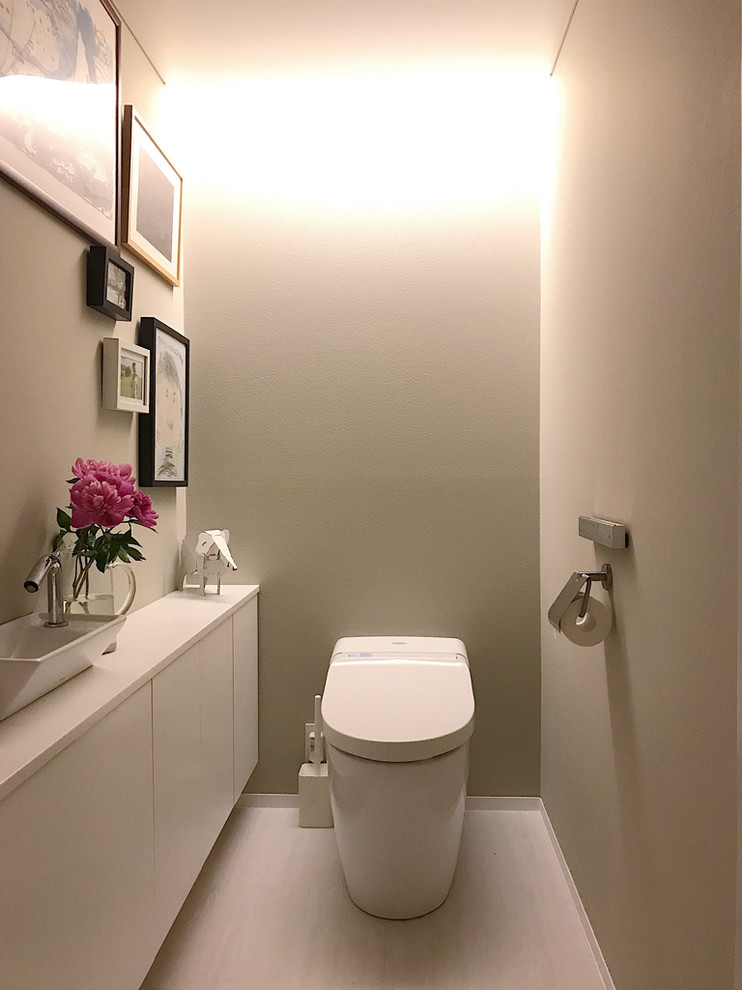東京23区にあるモダンスタイルのおしゃれなトイレ・洗面所 (フラットパネル扉のキャビネット、白いキャビネット、グレーの壁、ベッセル式洗面器、白い床、白い洗面カウンター) の写真