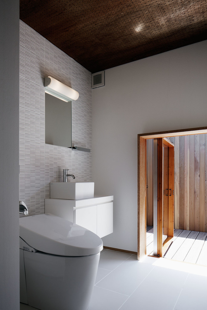 Пример оригинального дизайна: туалет в стиле модернизм с плоскими фасадами, белыми фасадами, белыми стенами, настольной раковиной, серым полом, унитазом-моноблоком, серой плиткой, керамогранитной плиткой и полом из керамогранита
