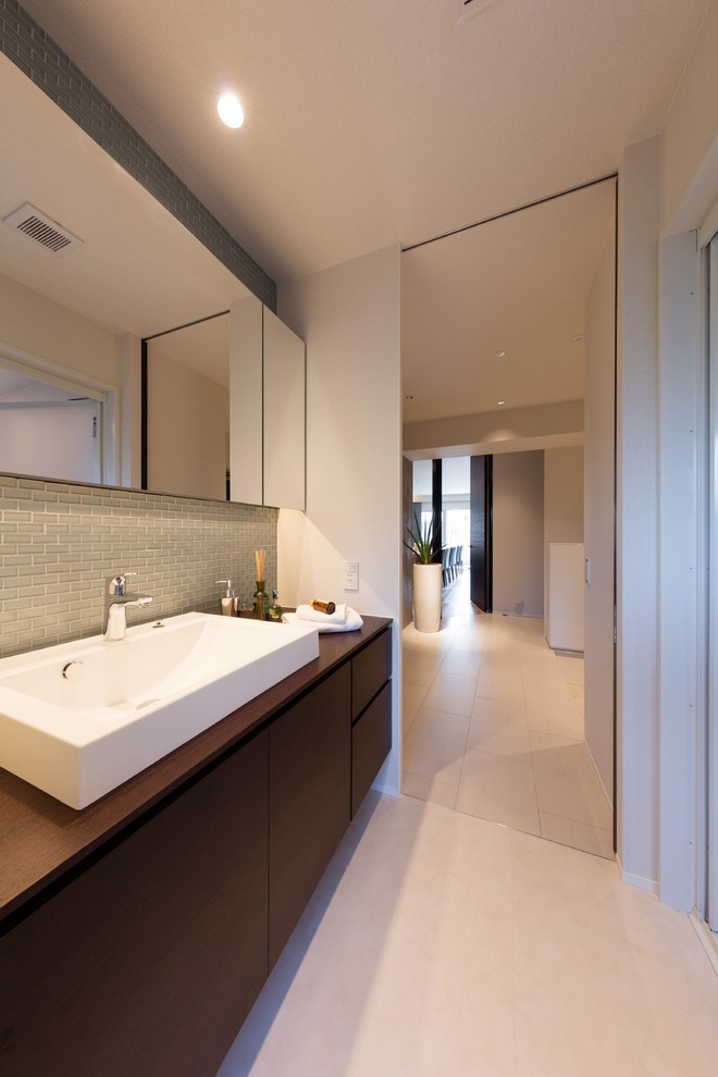 Cette image montre un WC et toilettes design en bois foncé avec un carrelage gris, un mur blanc, une vasque, un plan de toilette en bois, un sol beige et un plan de toilette marron.