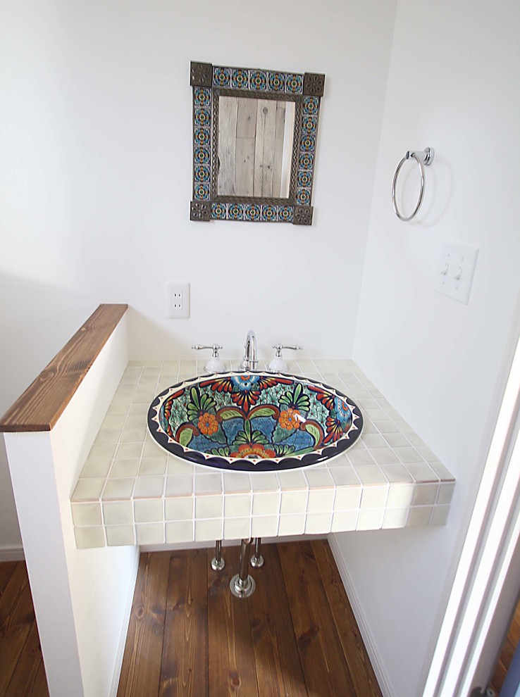 Immagine di un piccolo bagno di servizio tropicale con pareti bianche, pavimento in legno massello medio, lavabo da incasso, top piastrellato e piastrelle beige