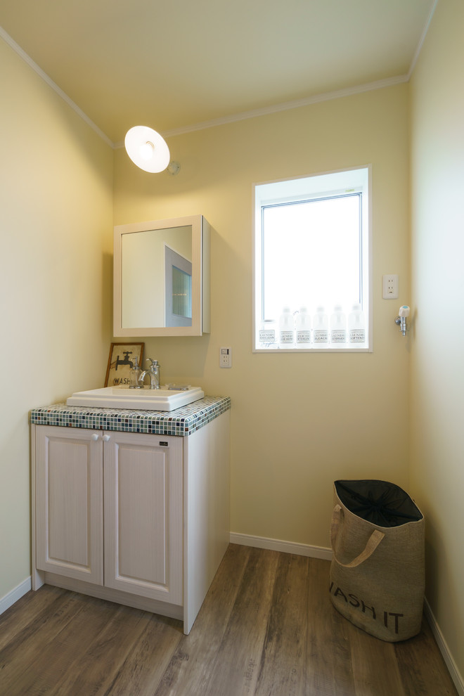 Photo of a coastal cloakroom in Other with raised-panel cabinets, yellow walls, dark hardwood flooring, a built-in sink, tiled worktops and brown floors.