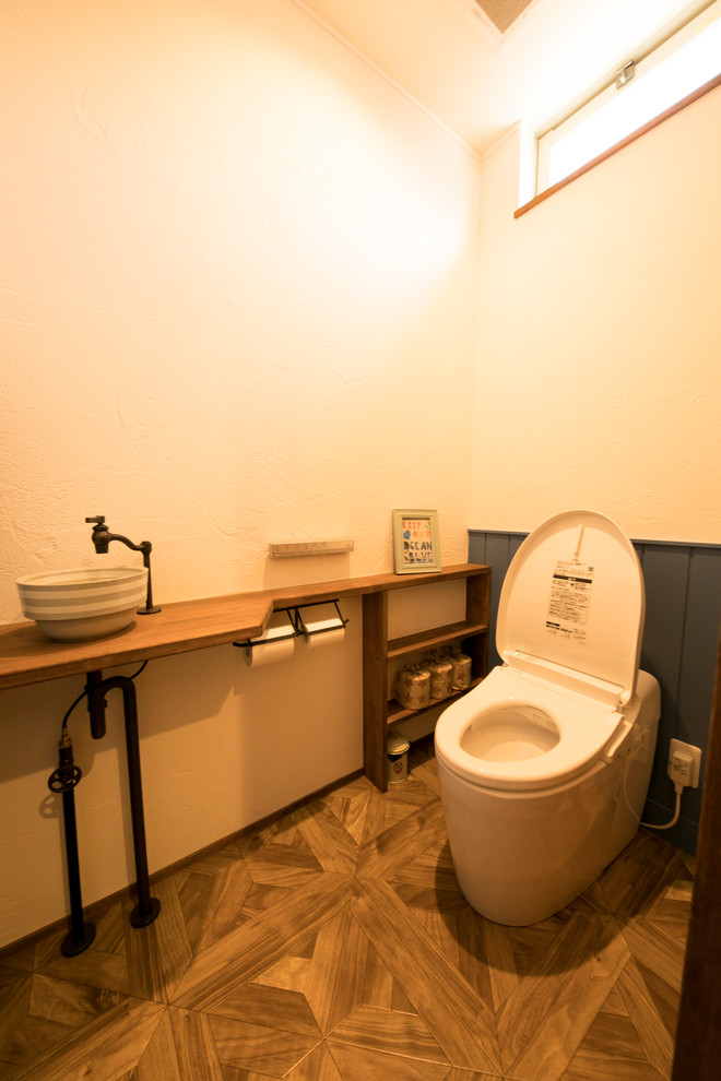 Aménagement d'un WC et toilettes bord de mer avec un mur blanc, un sol en bois brun, une vasque et un sol marron.