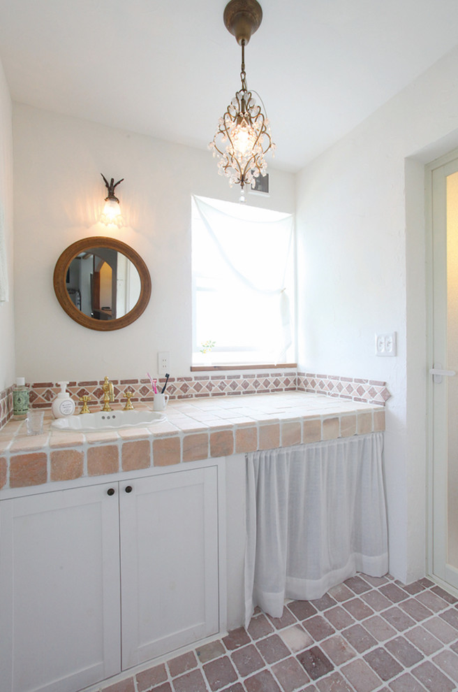 Inredning av ett medelhavsstil toalett, med luckor med infälld panel, vita skåp, vita väggar, ett nedsänkt handfat, kaklad bänkskiva och brunt golv