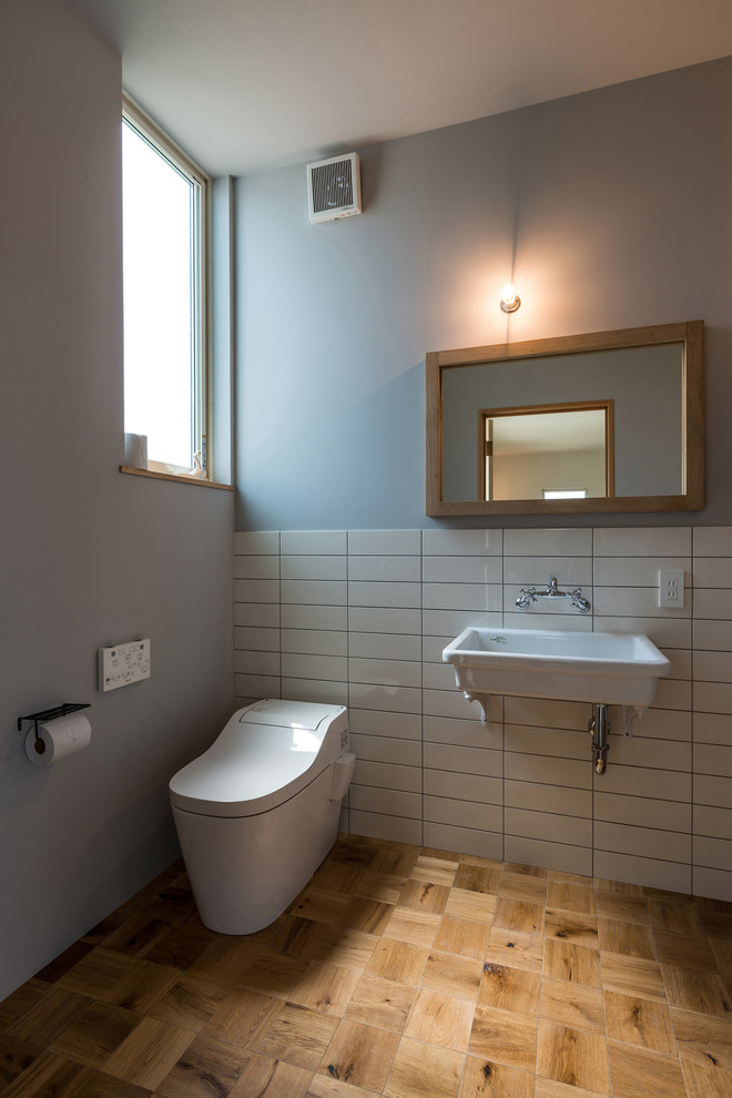 Ispirazione per un bagno di servizio costiero con WC monopezzo, piastrelle bianche, pavimento in legno massello medio e lavabo sospeso