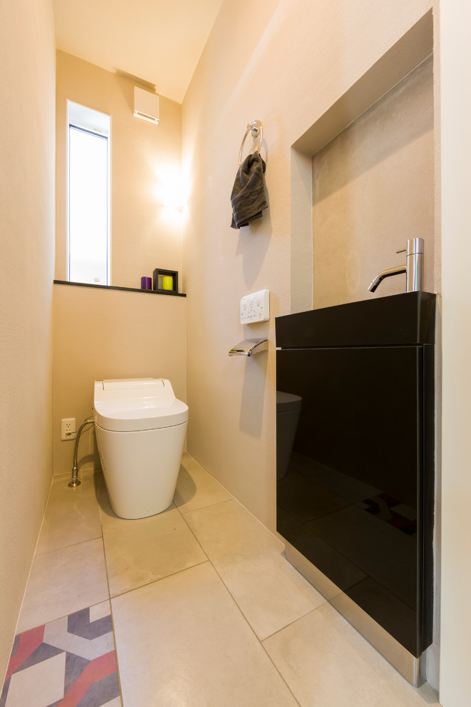 他の地域にある北欧スタイルのおしゃれなトイレ・洗面所 (黒いキャビネット、一体型トイレ	、ベージュの壁、磁器タイルの床、ベージュの床、黒い洗面カウンター) の写真