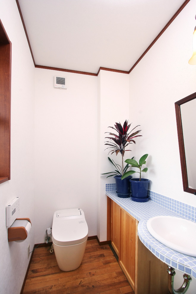 Mid-Century Gästetoilette mit hellbraunen Holzschränken, weißer Wandfarbe, braunem Holzboden, Einbauwaschbecken, gefliestem Waschtisch und braunem Boden in Sonstige