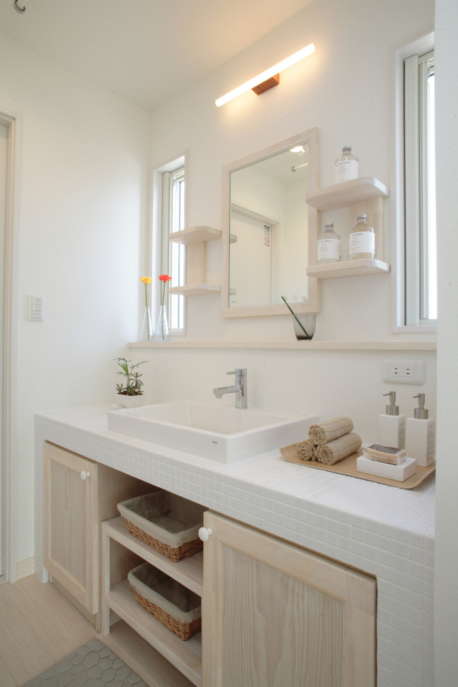 Inredning av ett modernt stort vit vitt toalett, med luckor med profilerade fronter, vita skåp, vit kakel, keramikplattor, vita väggar, linoleumgolv, ett fristående handfat, kaklad bänkskiva och beiget golv