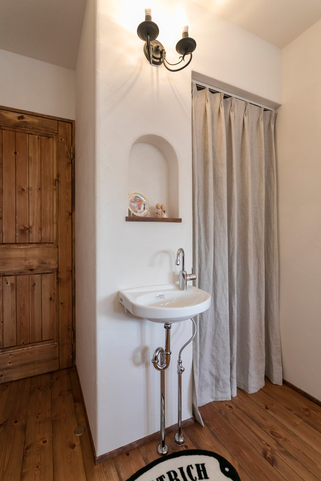 Ispirazione per un bagno di servizio etnico con pareti bianche, pavimento marrone, pavimento in legno massello medio e lavabo sospeso