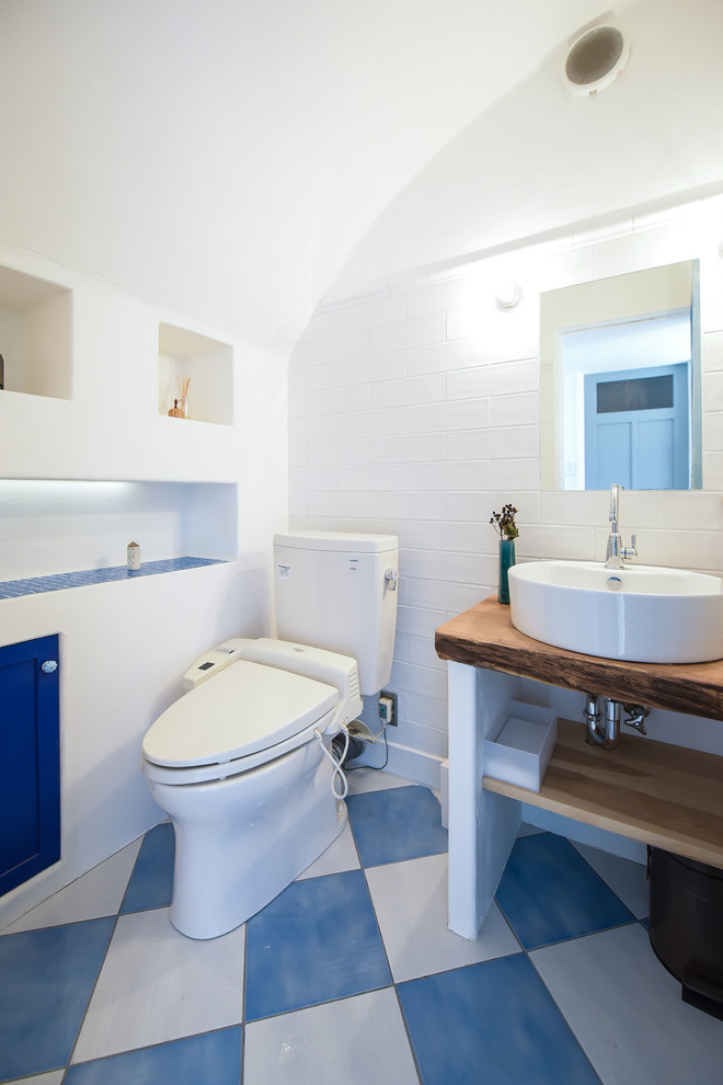 Foto på ett medelhavsstil toalett, med öppna hyllor, ett fristående handfat, träbänkskiva och flerfärgat golv
