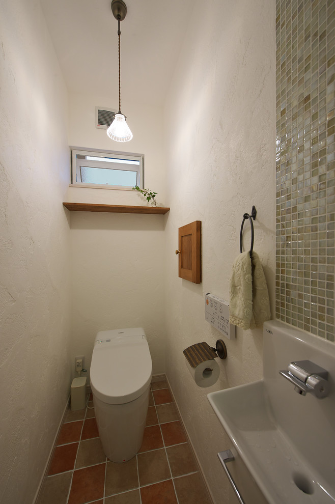 他の地域にあるカントリー風のおしゃれなトイレ・洗面所 (一体型トイレ	、白い壁、磁器タイルの床、マルチカラーの床) の写真