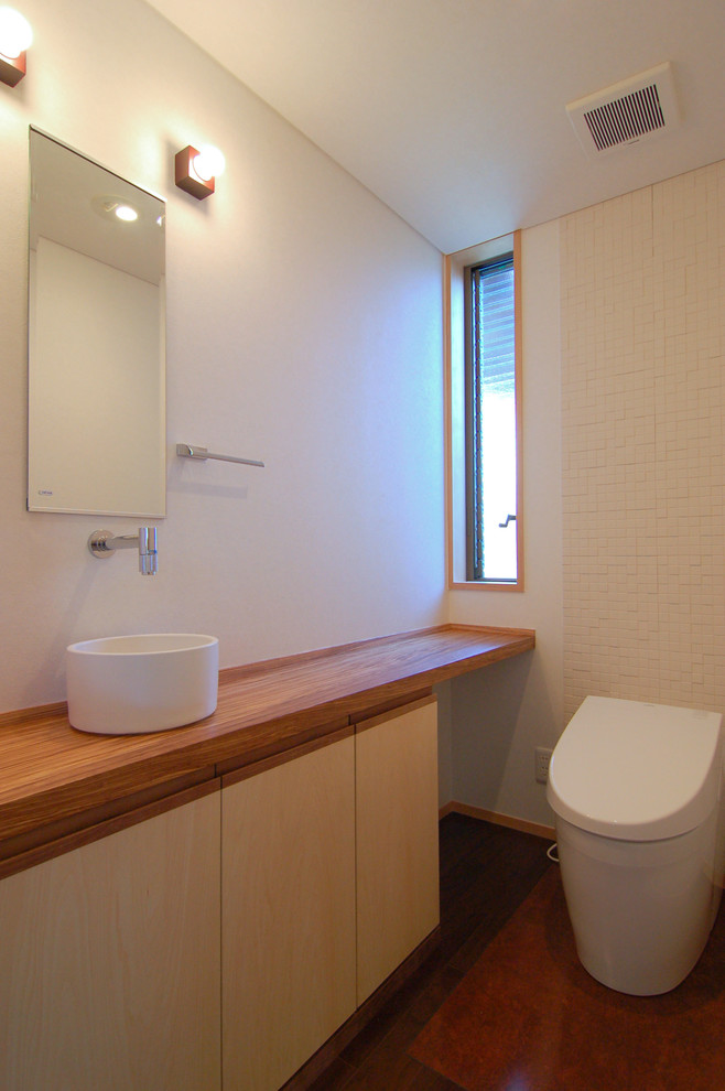 Exemple d'un WC et toilettes asiatique avec des portes de placard beiges, un carrelage blanc, un mur blanc, un sol en carrelage de céramique, un plan de toilette en bois, un sol marron, une vasque et un plan de toilette marron.
