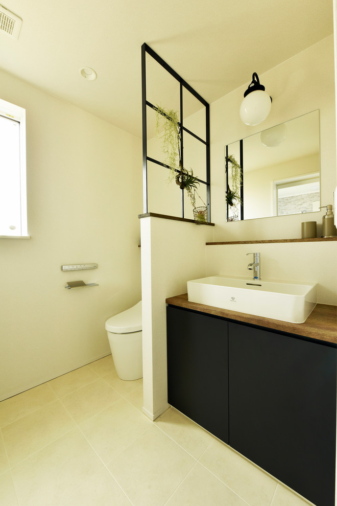 Moderne Gästetoilette mit Kassettenfronten, schwarzen Schränken, Toilette mit Aufsatzspülkasten, weißer Wandfarbe, Vinylboden, Aufsatzwaschbecken, Waschtisch aus Holz und beigem Boden in Sonstige