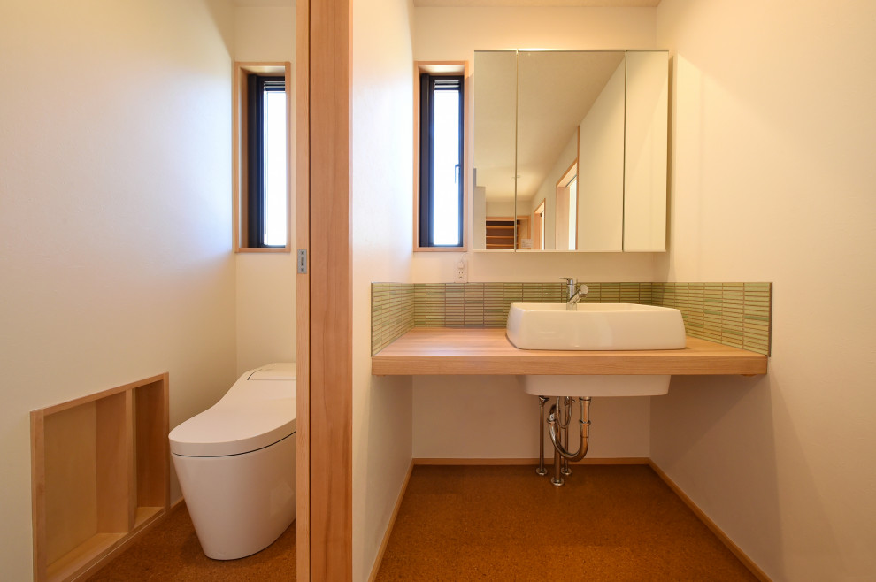 На фото: туалет с белыми фасадами, унитазом-моноблоком, зеленой плиткой, пробковым полом, коричневым полом, потолком с обоями и обоями на стенах