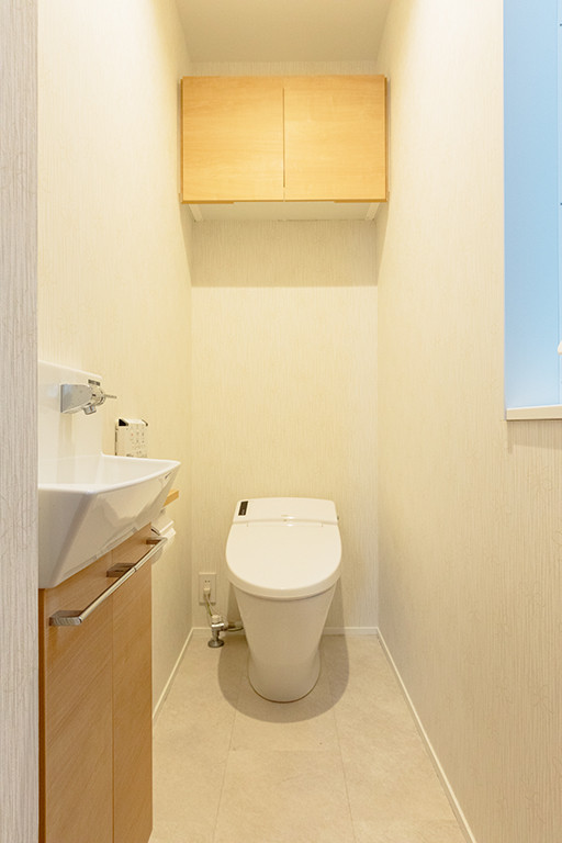 Bild på ett mellanstort funkis brun brunt toalett, med släta luckor, vita skåp, en toalettstol med hel cisternkåpa, vita väggar, ett väggmonterat handfat, bänkskiva i akrylsten, vitt golv och klinkergolv i porslin
